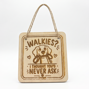 A square wooden hanging plaque with a twine handle, featuring a cartoon dog and the text 'WALKIES? I THOUGHT YOU'D NEVER ASK'.